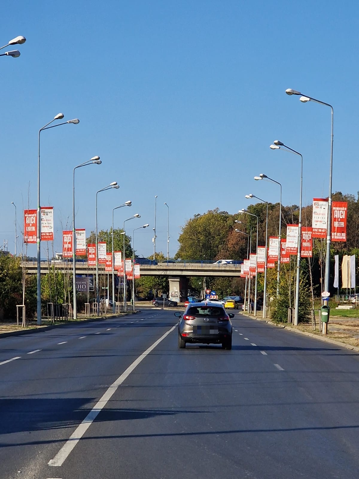 Șir de steaguri direcționale roșii și albe montate în perechi pe stâlpii de iluminat, pe ambele părți ale unei artere urbane cu patru benzi